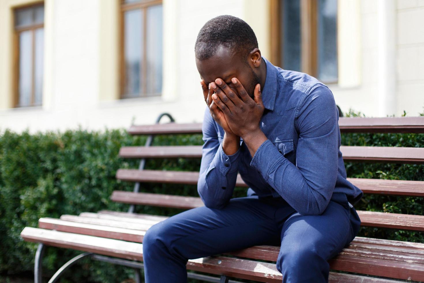 Tired African American man sits on the bench outside photo