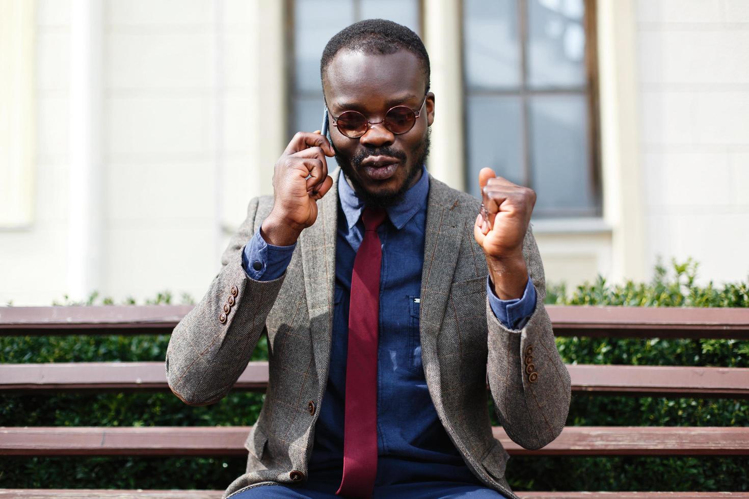 African American man talks on the smartphone sitting on the bench outside photo