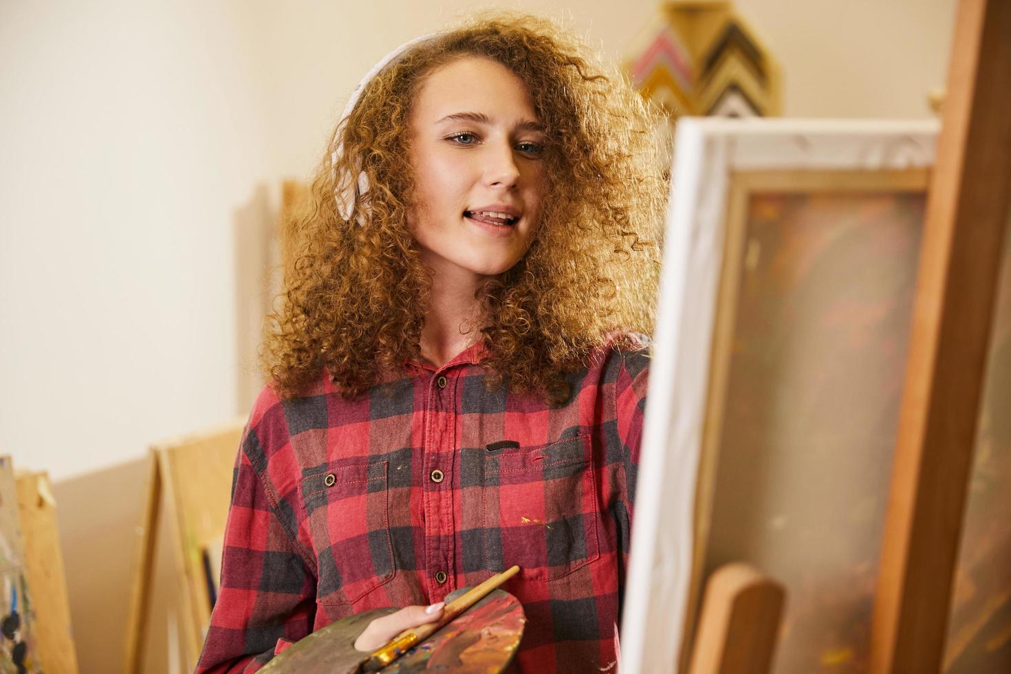 Beautiful girl listens to music via headphones and singing while painting photo