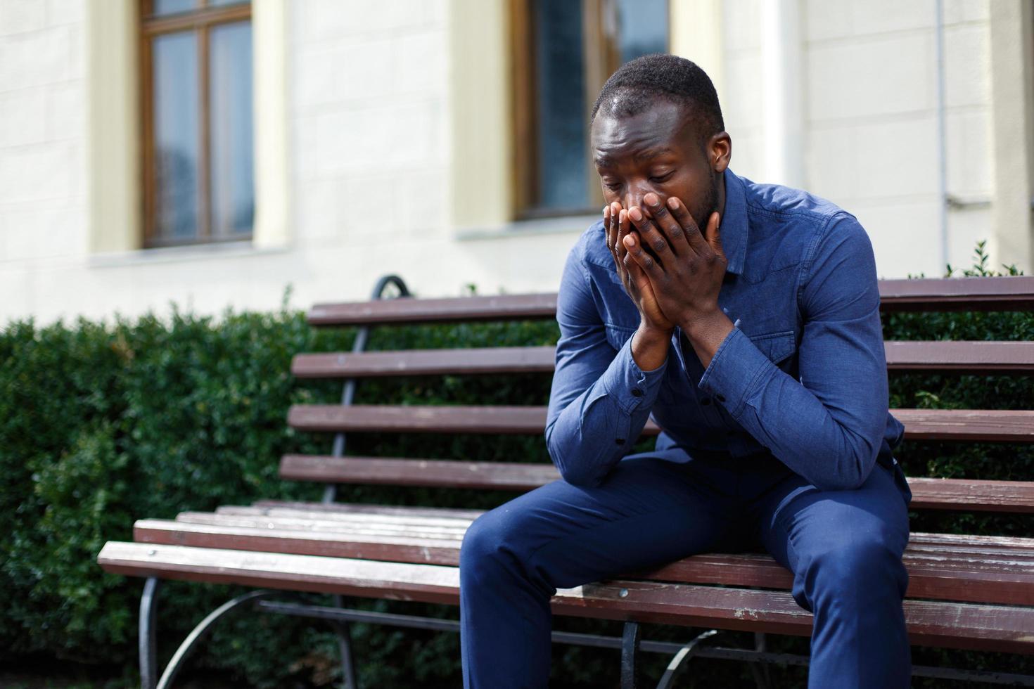 Hombre afroamericano cansado se sienta en el banco fuera foto