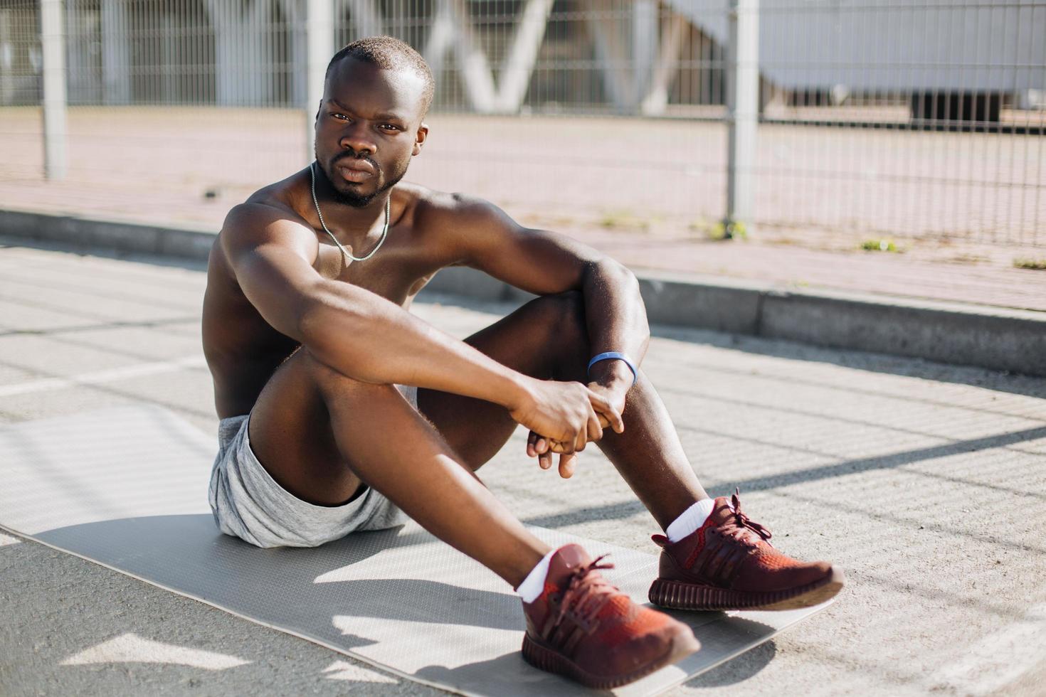 African American man sits tired on the ground after doing his exercises photo