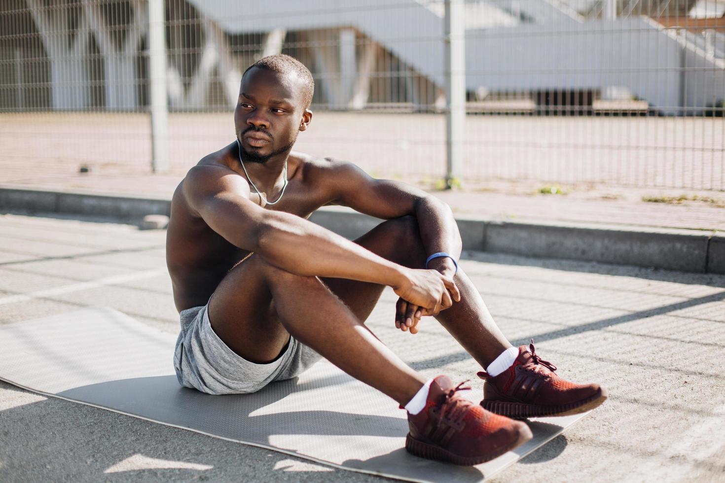 African American man sits tired on the ground after doing his exercises photo