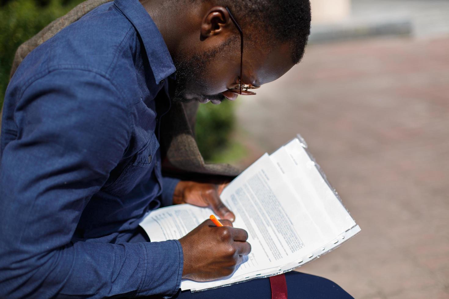 Hombre afroamericano firma papeles sentado en el banco fuera foto