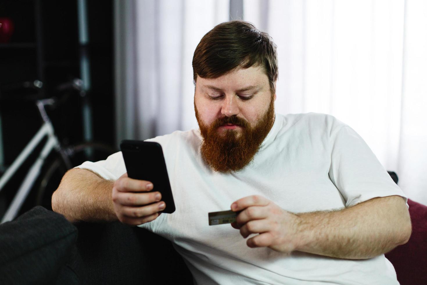 Fat man types the number of a credit card in his phone photo