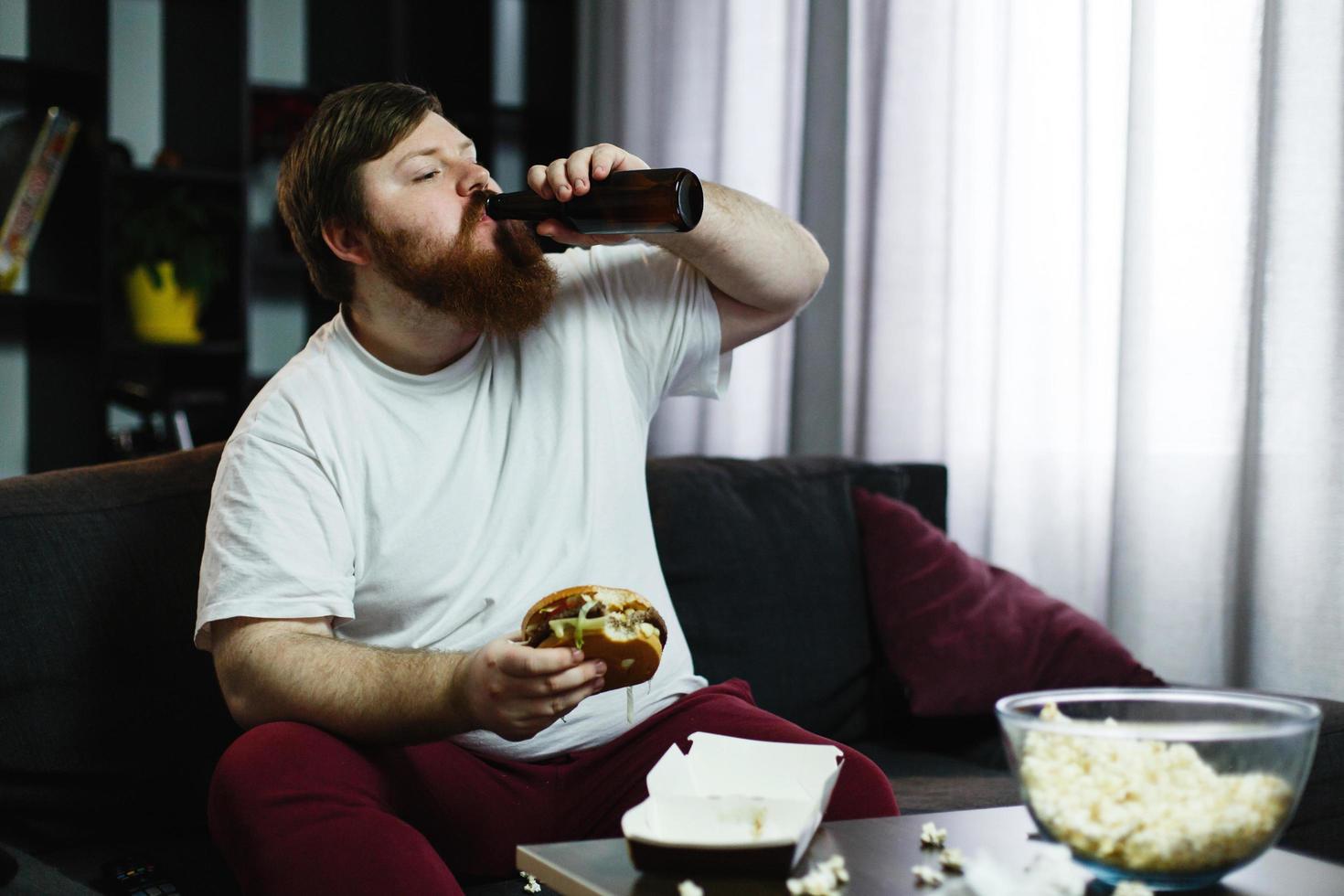 hombre gordo come hamburguesa con cerveza sentado en la mesa foto