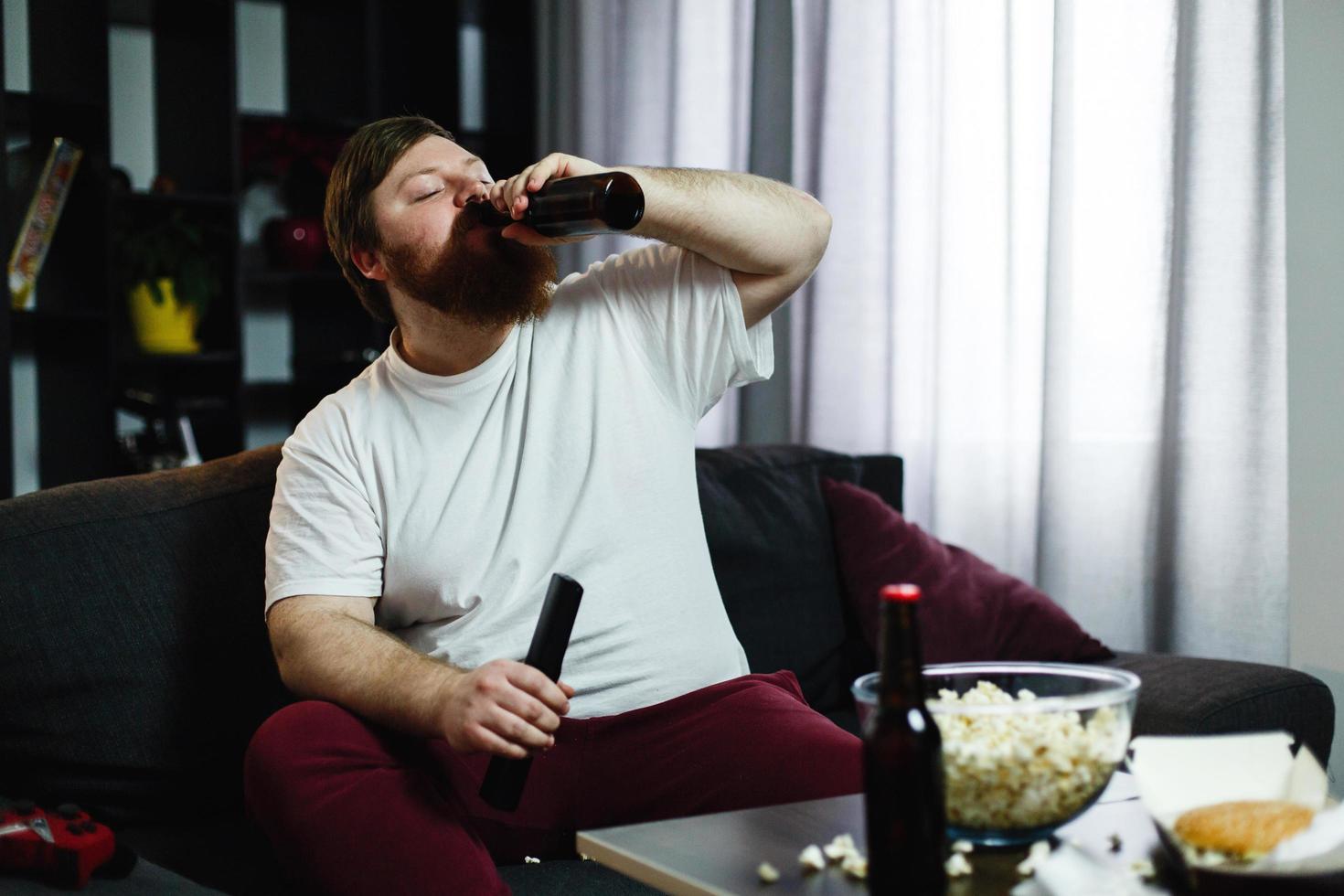 hombre gordo bebe cerveza acostado en el sofá foto