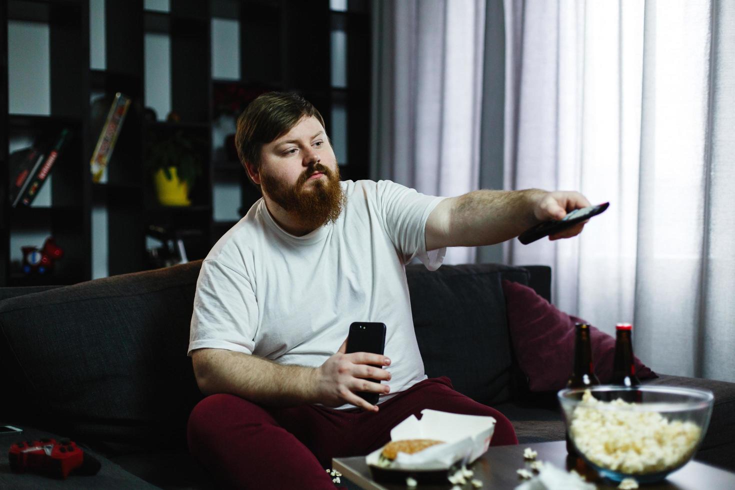 El hombre cambia los canales de la televisión sentado en el sofá. foto