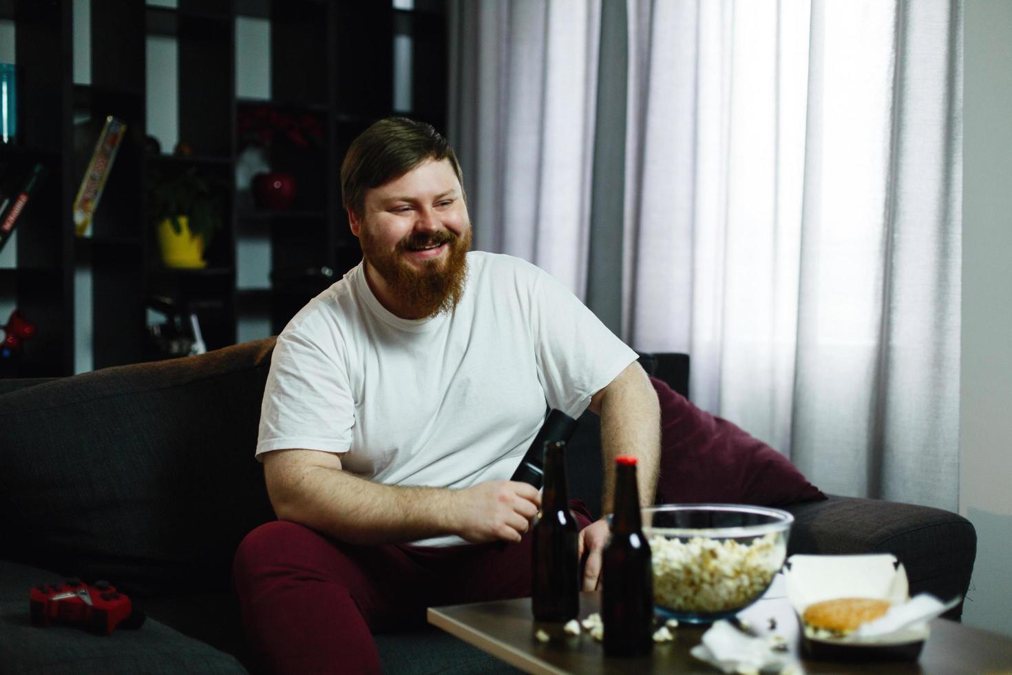 hombre gordo feliz se sienta en el sofá y ve la televisión foto