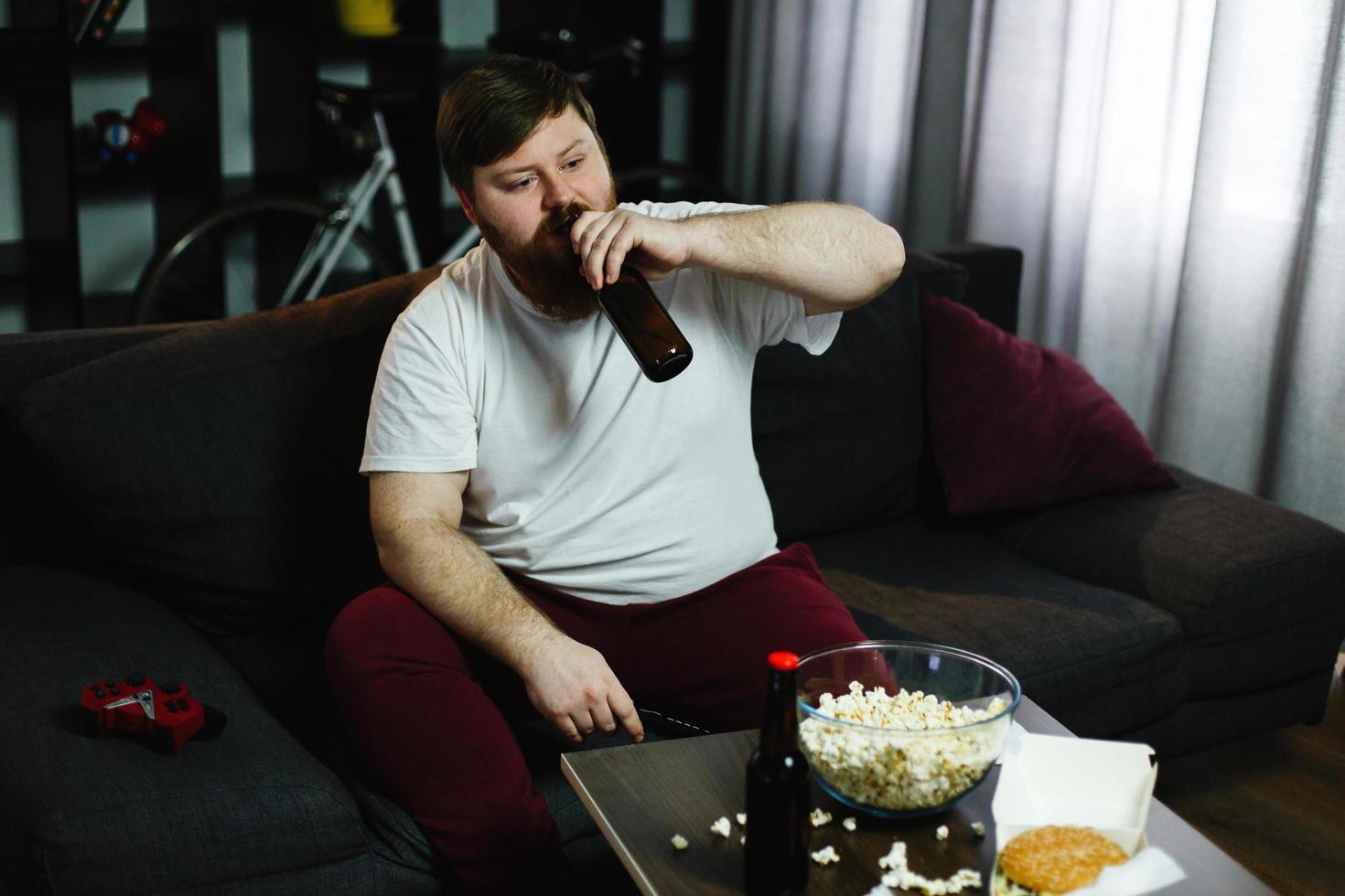 hombre gordo bebe cerveza acostado en el sofá foto