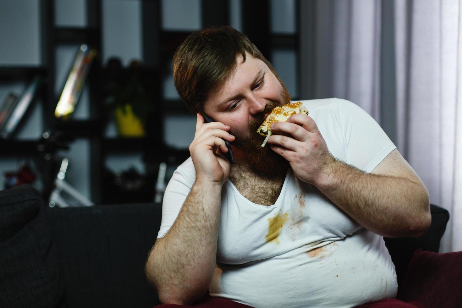 hombre comiendo una hamburguesa mientras habla por teléfono foto