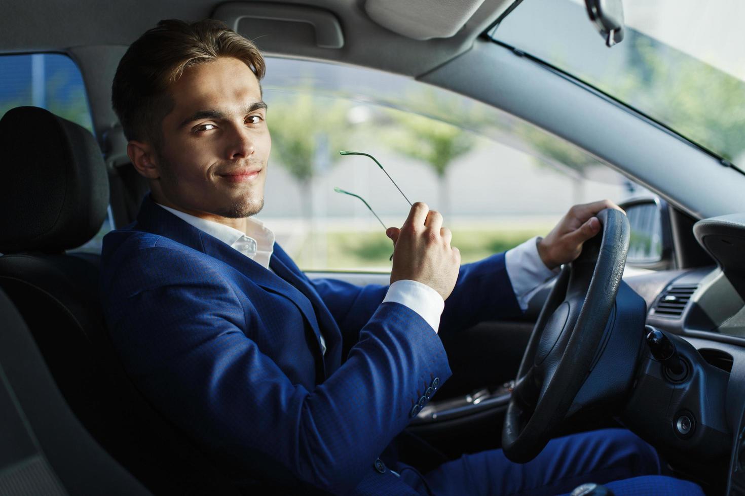 apuesto joven empresario se sienta al volante dentro del coche foto