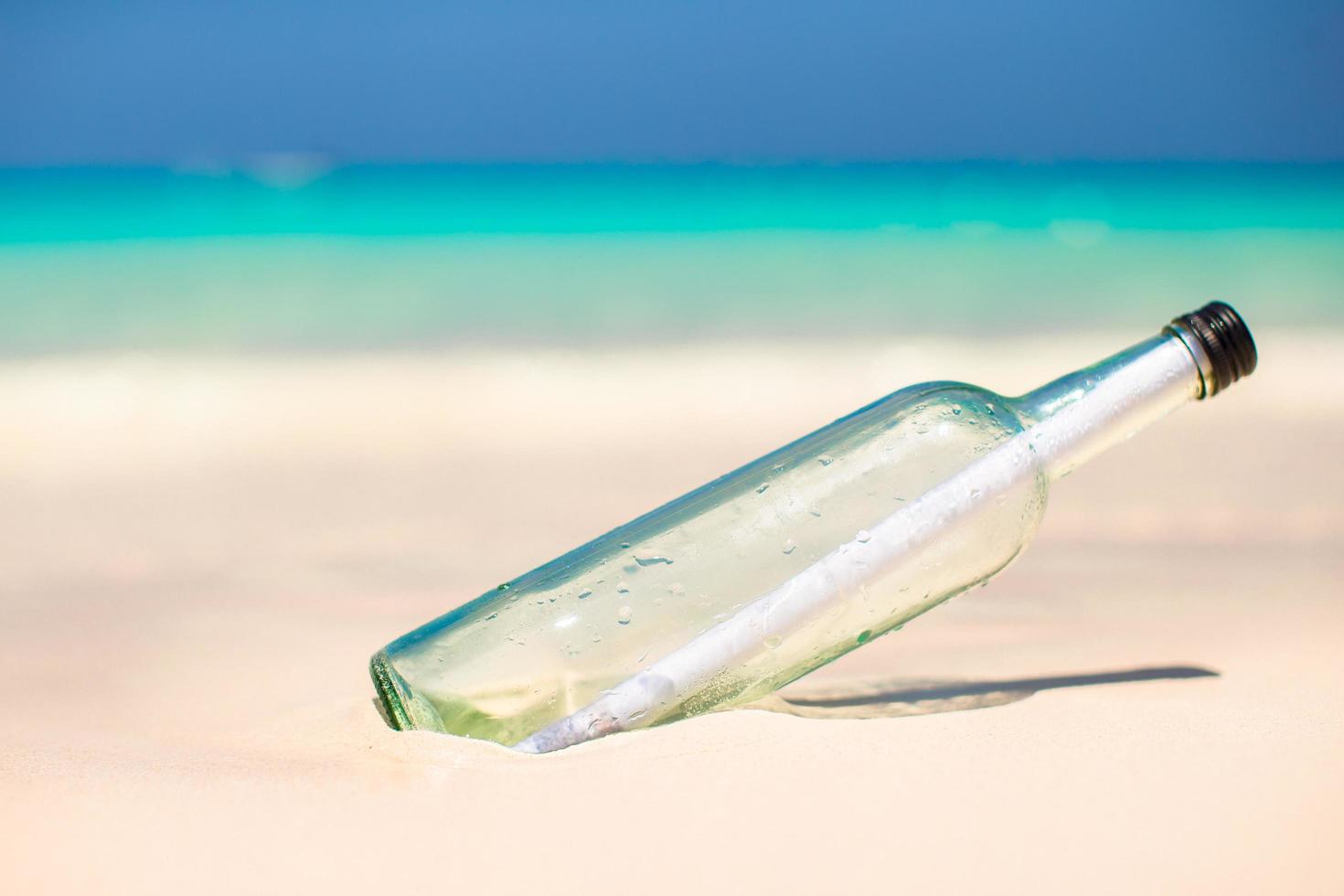 Botella de vidrio con un mensaje en la playa foto