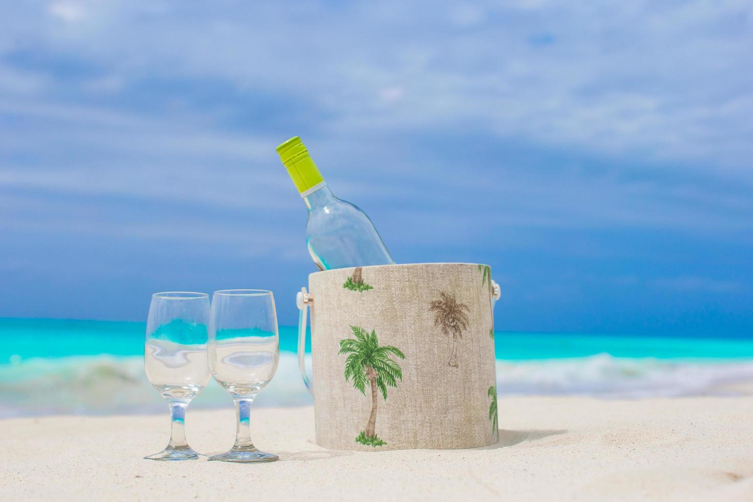 botella de vino blanco y dos copas en la playa foto