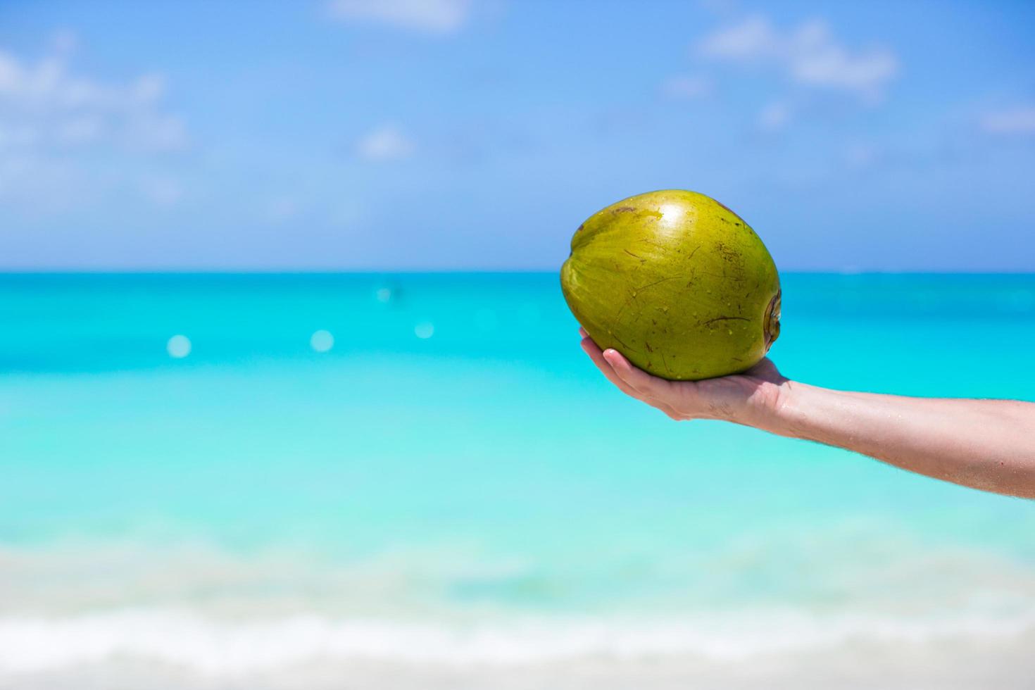 persona sosteniendo un coco en una playa tropical foto