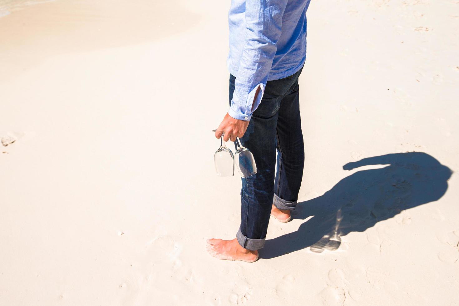 Hombre sujetando copas de vino en la playa foto
