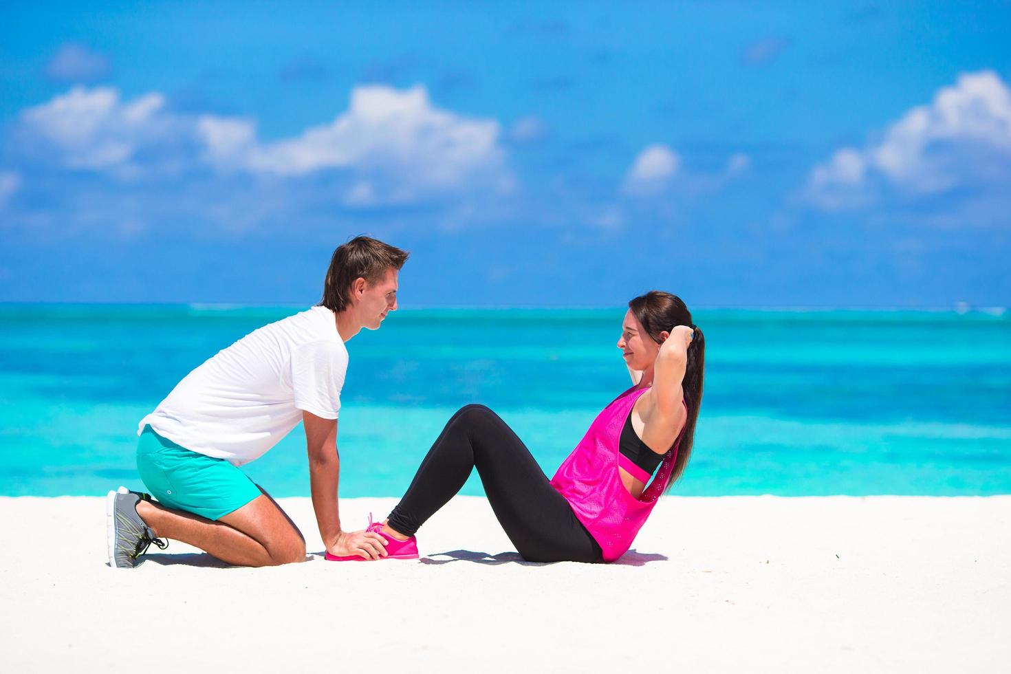 Man spotting woman while doing crunches on a beach photo