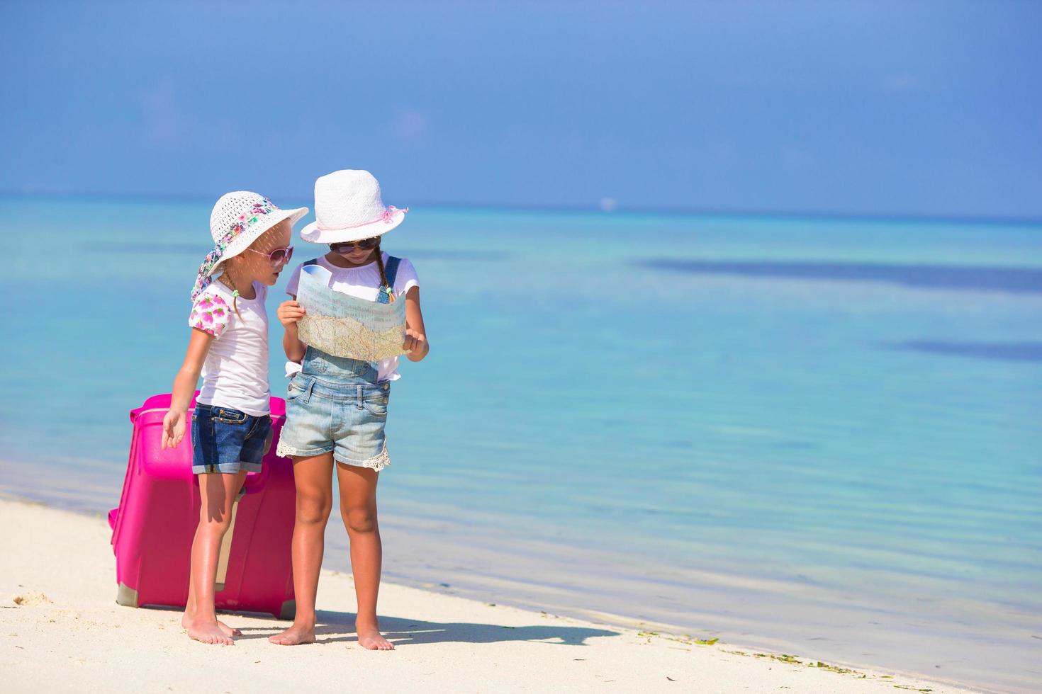 dos niñas con un mapa y equipaje en la playa foto