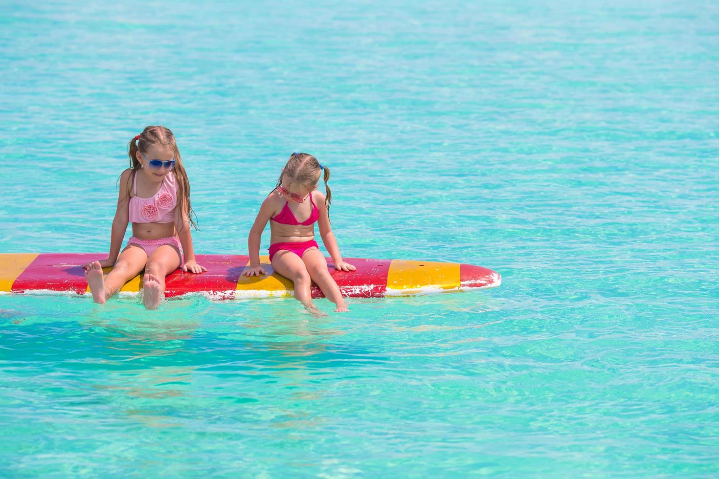 Two girls sitting on a surfboard photo