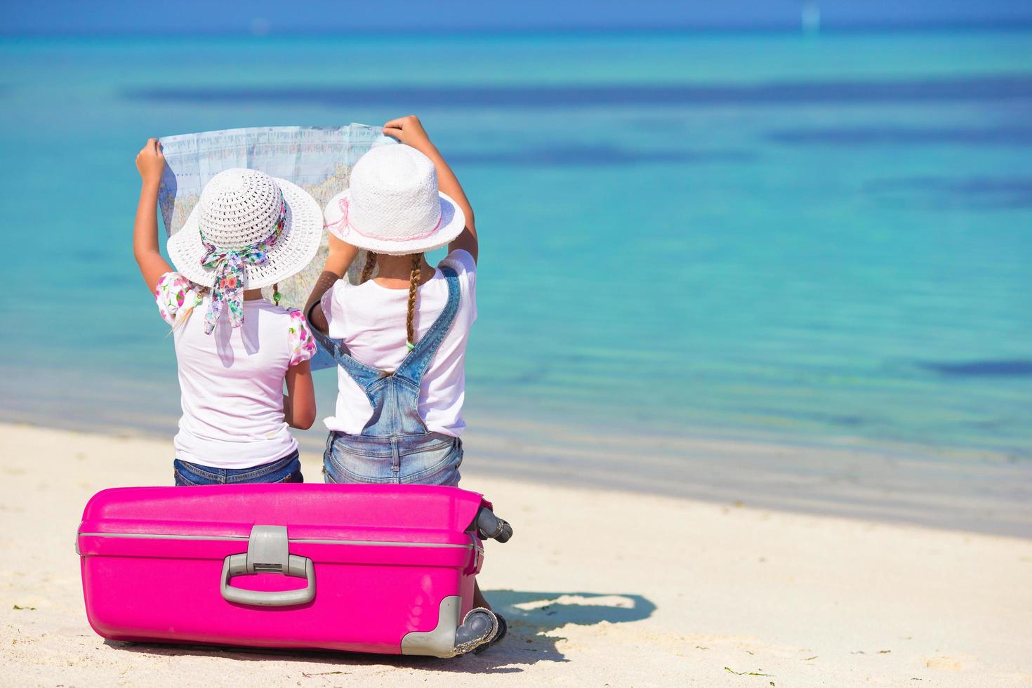 Dos niñas mirando un mapa mientras están sentados en el equipaje en la playa. foto