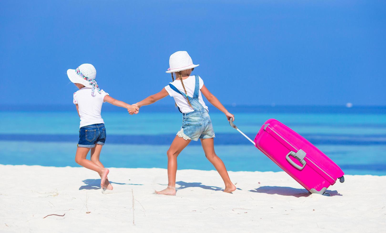 Two girls walking on a beach with luggage photo