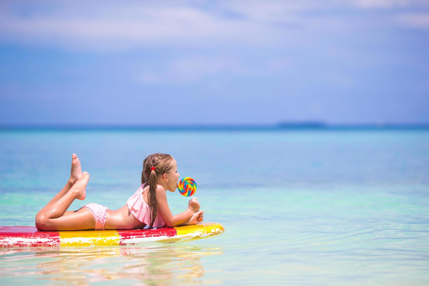 Girl with a lollipop on a surfboard in the sea photo