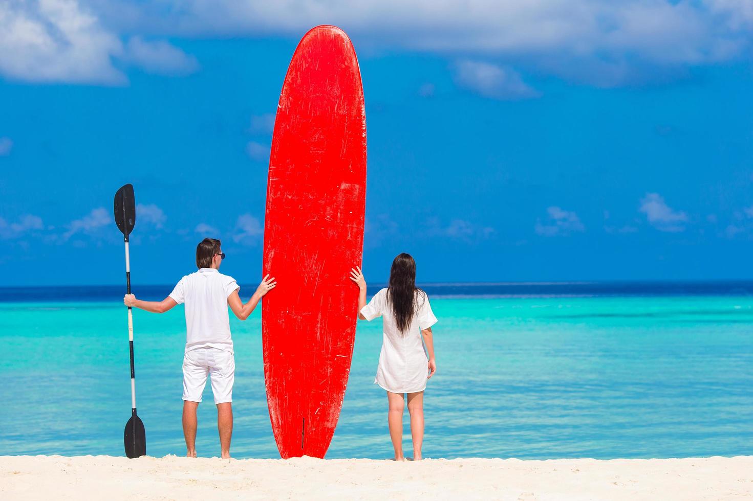 dos personas de pie en una playa con una tabla de remo foto