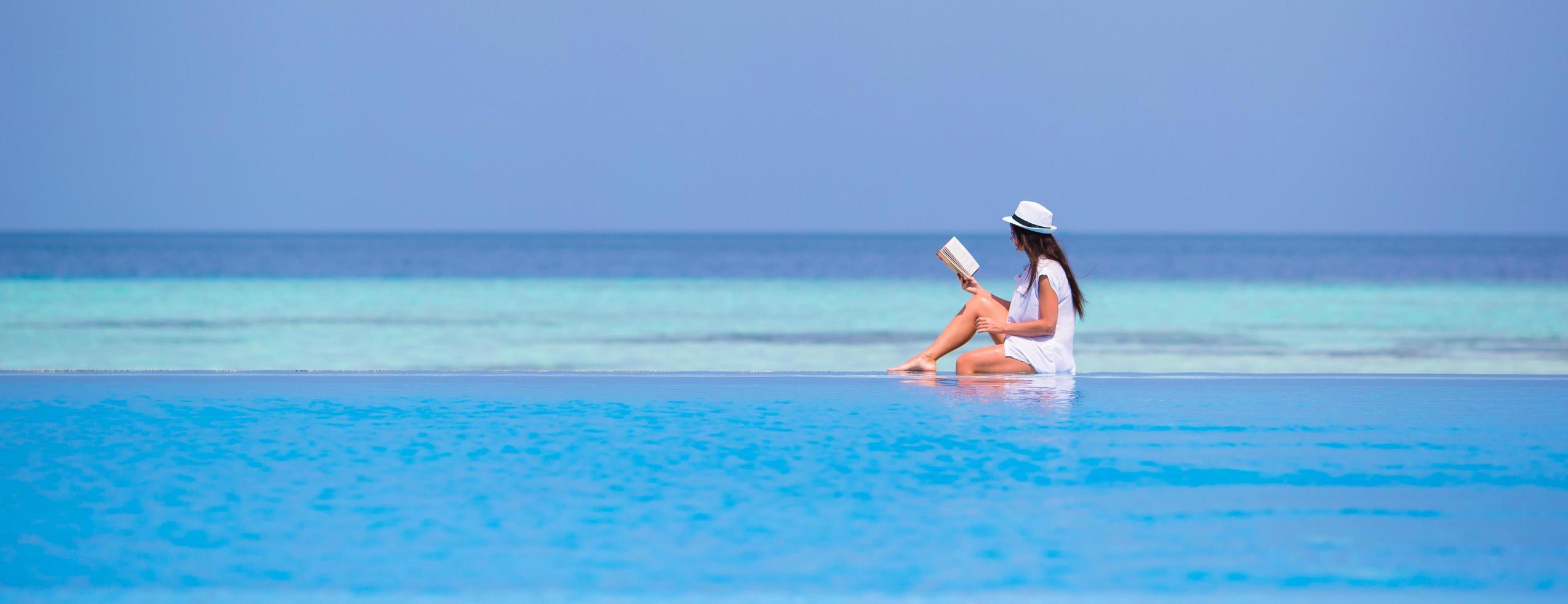 Woman reading a book while sitting on the edge of a swimming pool photo