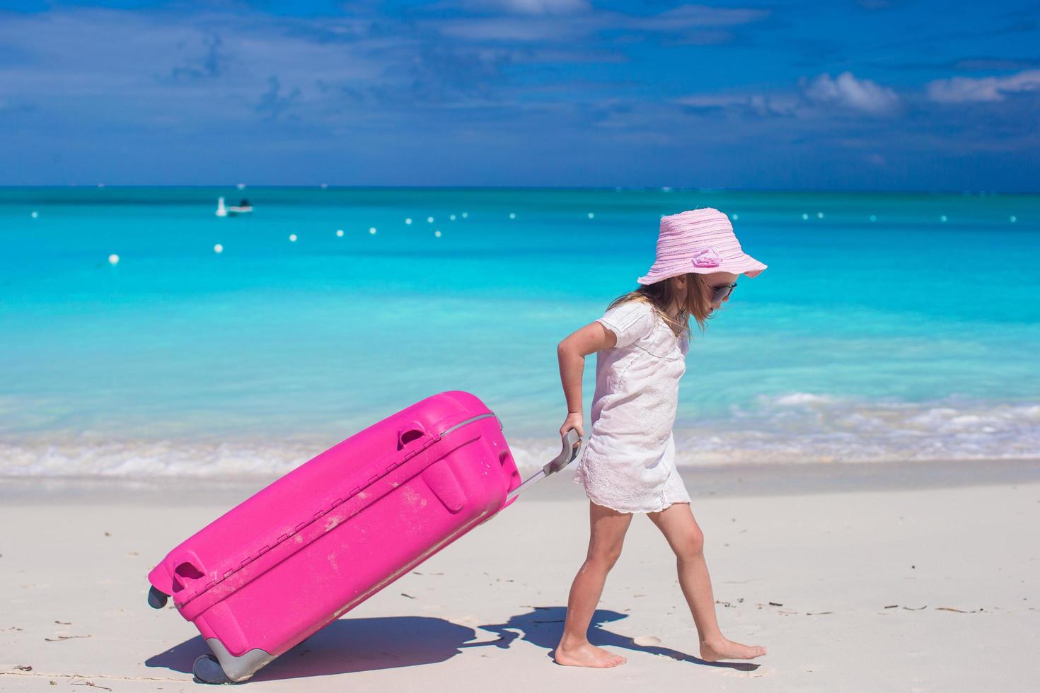 chica con maleta rosa caminando en la playa foto