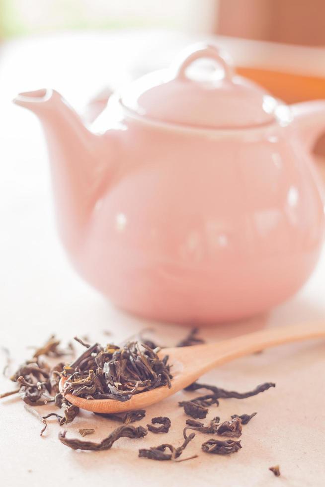 té seco en una cuchara de madera con una jarra de cerámica foto