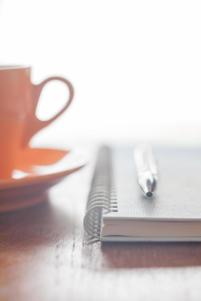Taza de café naranja con un bolígrafo y un cuaderno sobre una mesa de madera foto