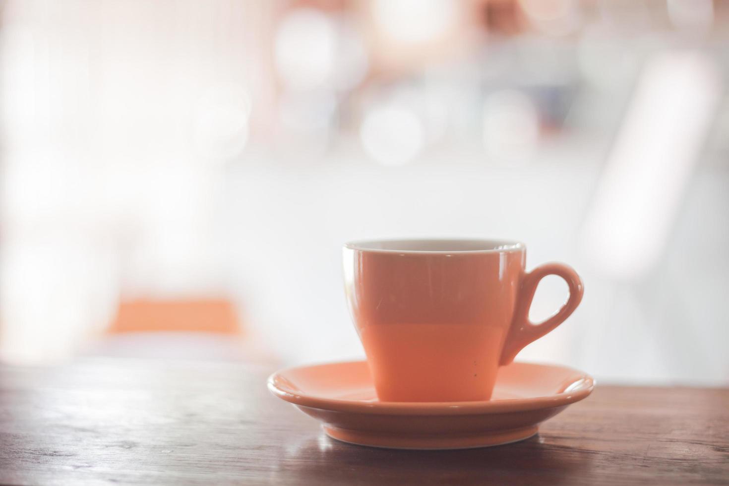 Taza de café naranja sobre una mesa de madera foto