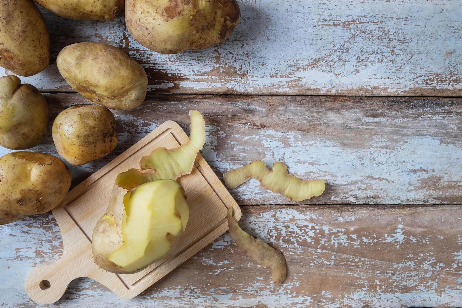 Las patatas se pelan sobre fondo de madera foto