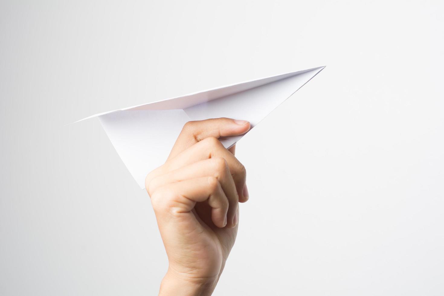 La mano de una mujer sostiene un avión de papel sobre fondo blanco. foto