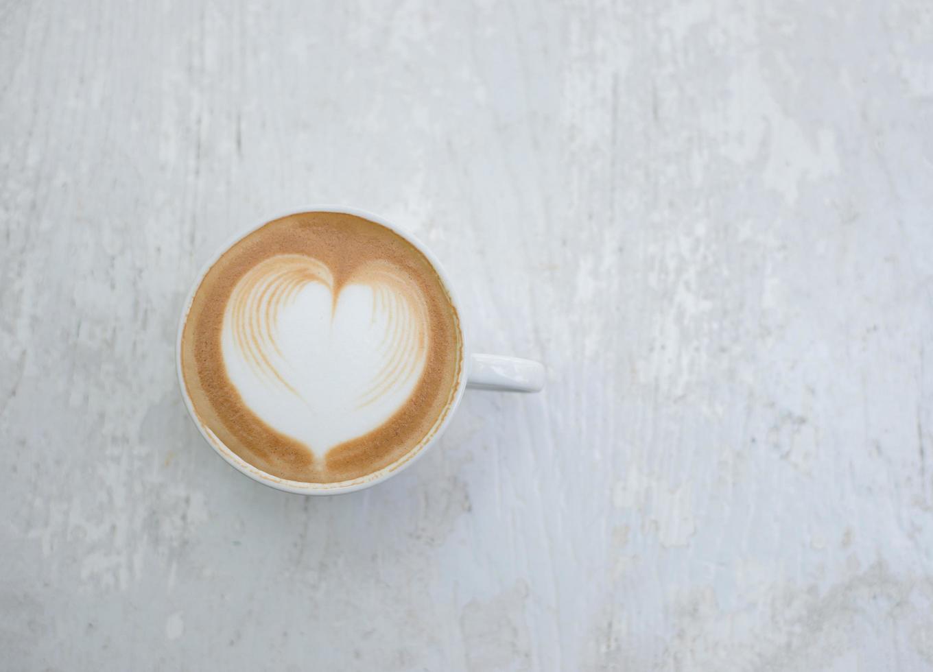 Cup of latte with heart shape on white table photo