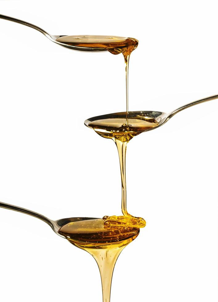 Honey falling on metal spoons with a white background photo