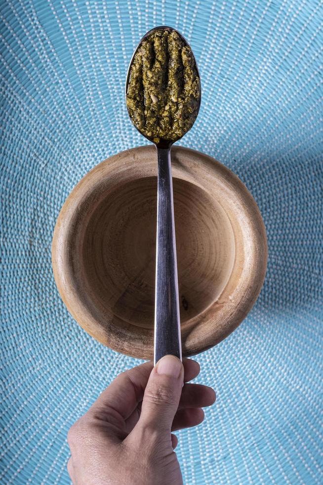 Pesto spoon on a wooden bowl on a light blue background photo