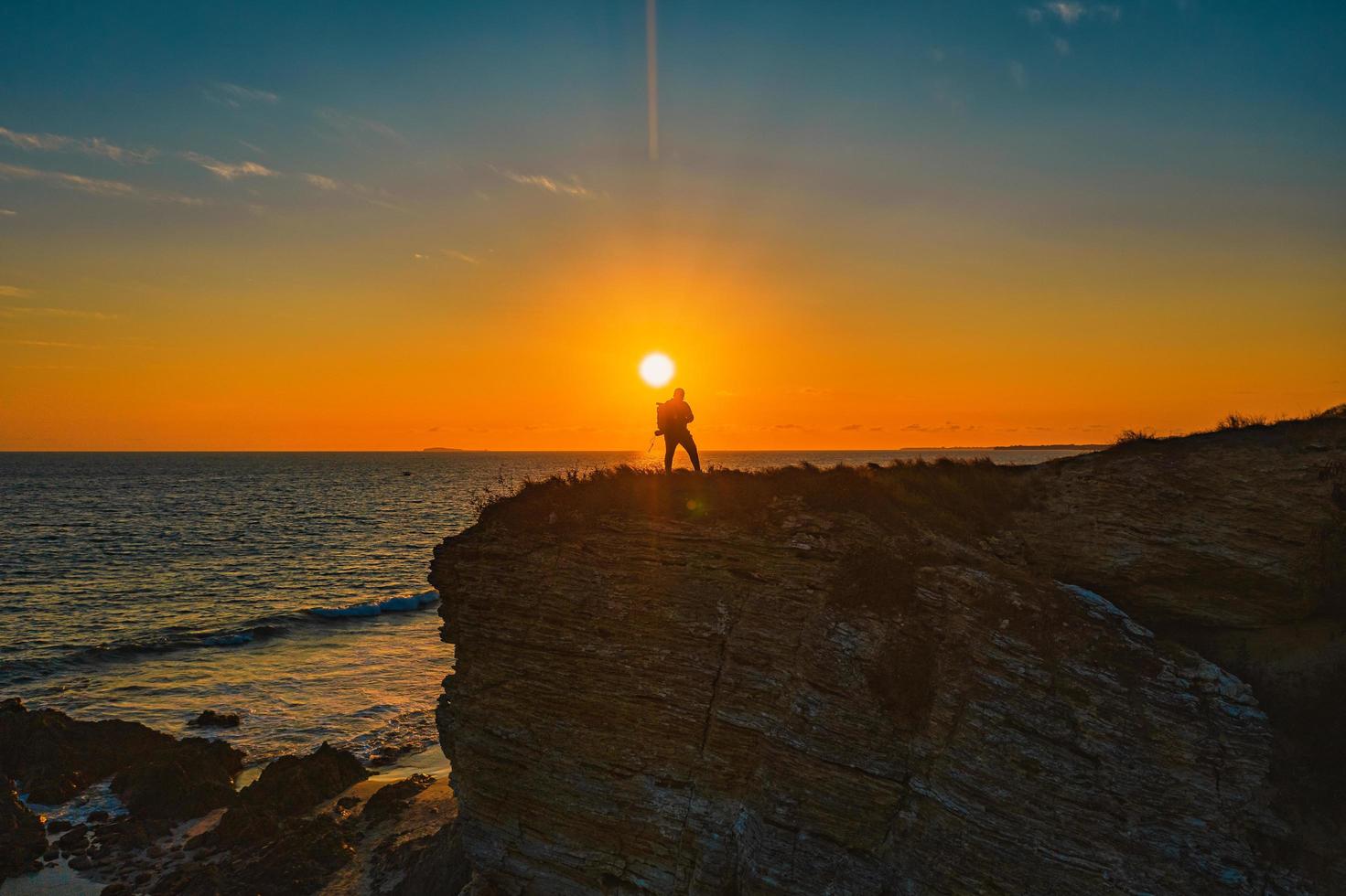 Persona de pie sobre una formación rocosa cerca del mar durante la puesta de sol foto