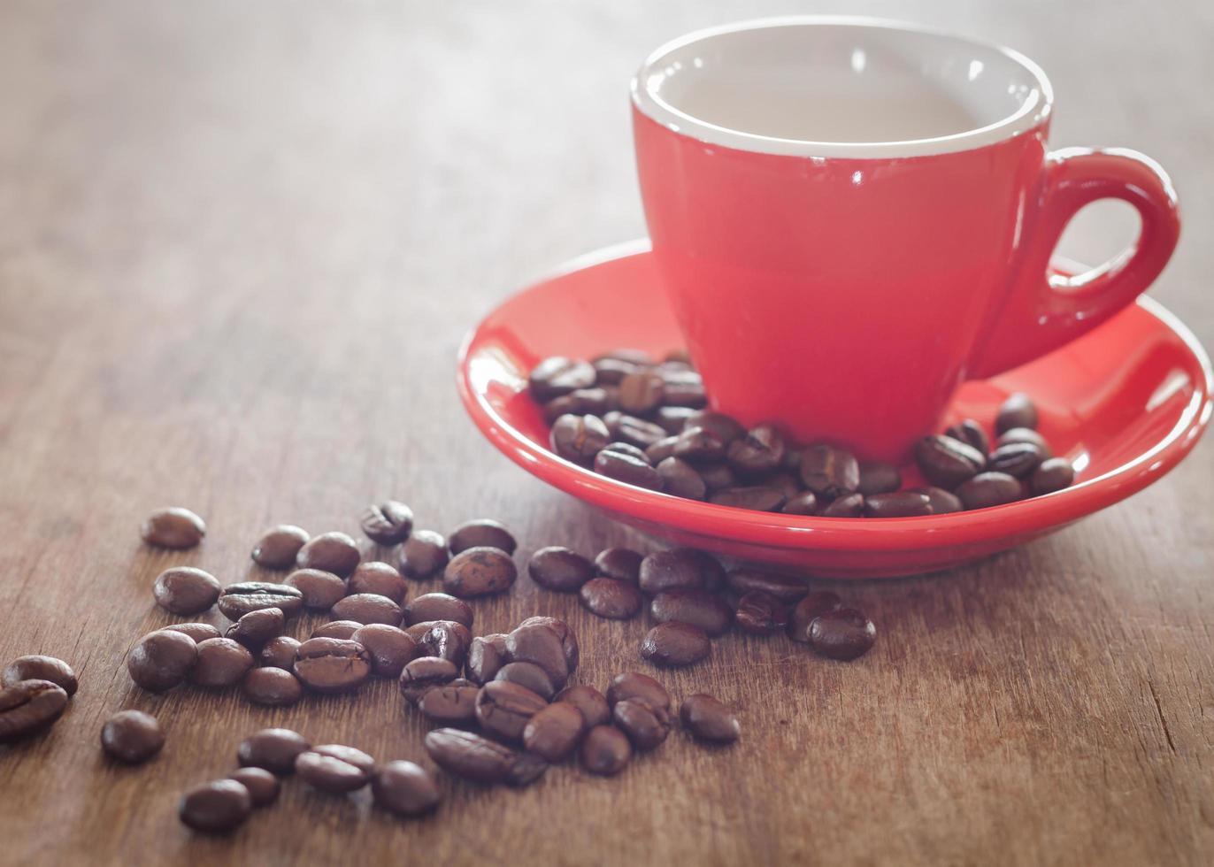 Close-up de una taza de café rojo con granos de café sobre una mesa de madera foto