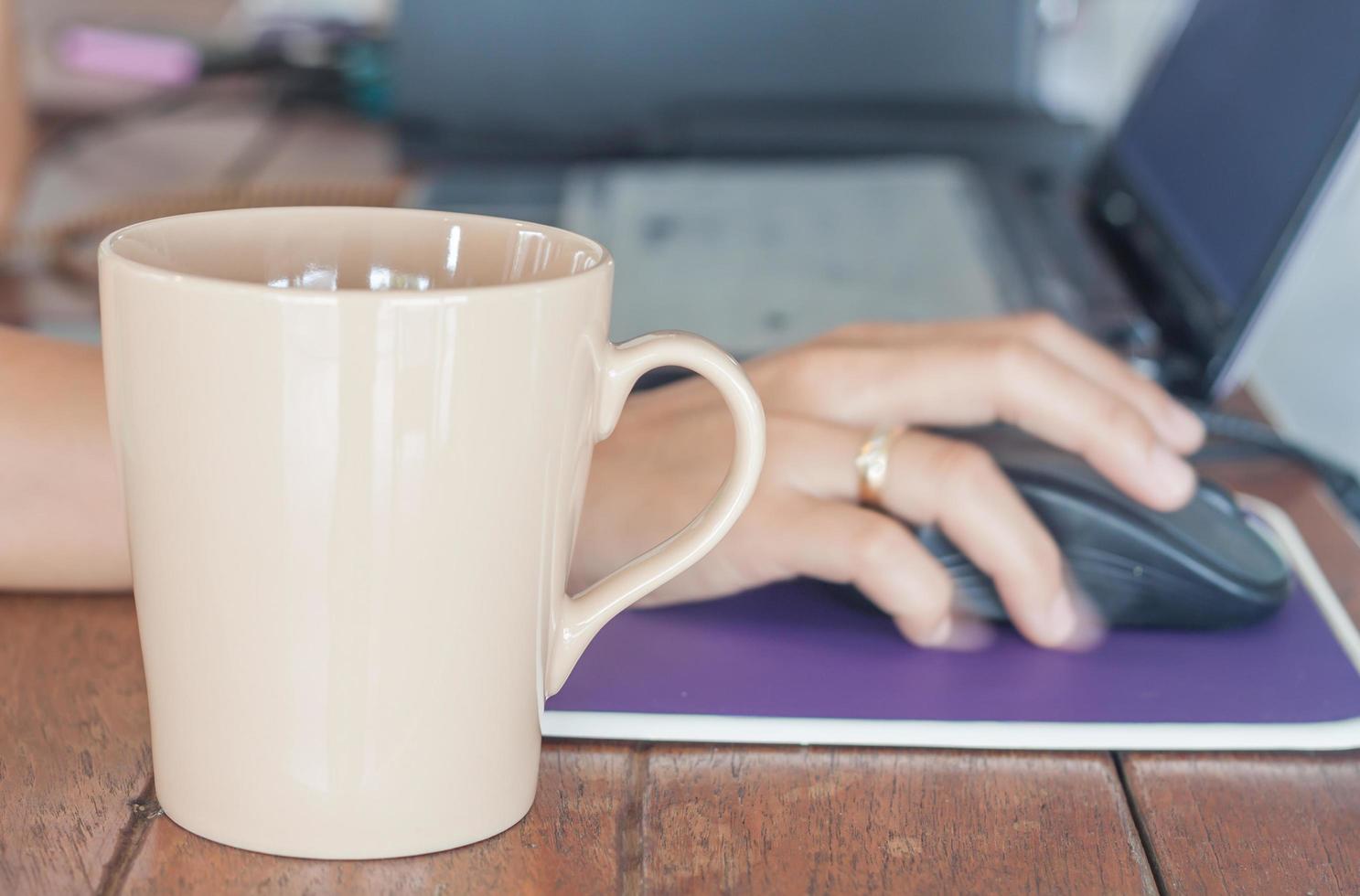 Coffee mug in front of a person working on a laptop photo