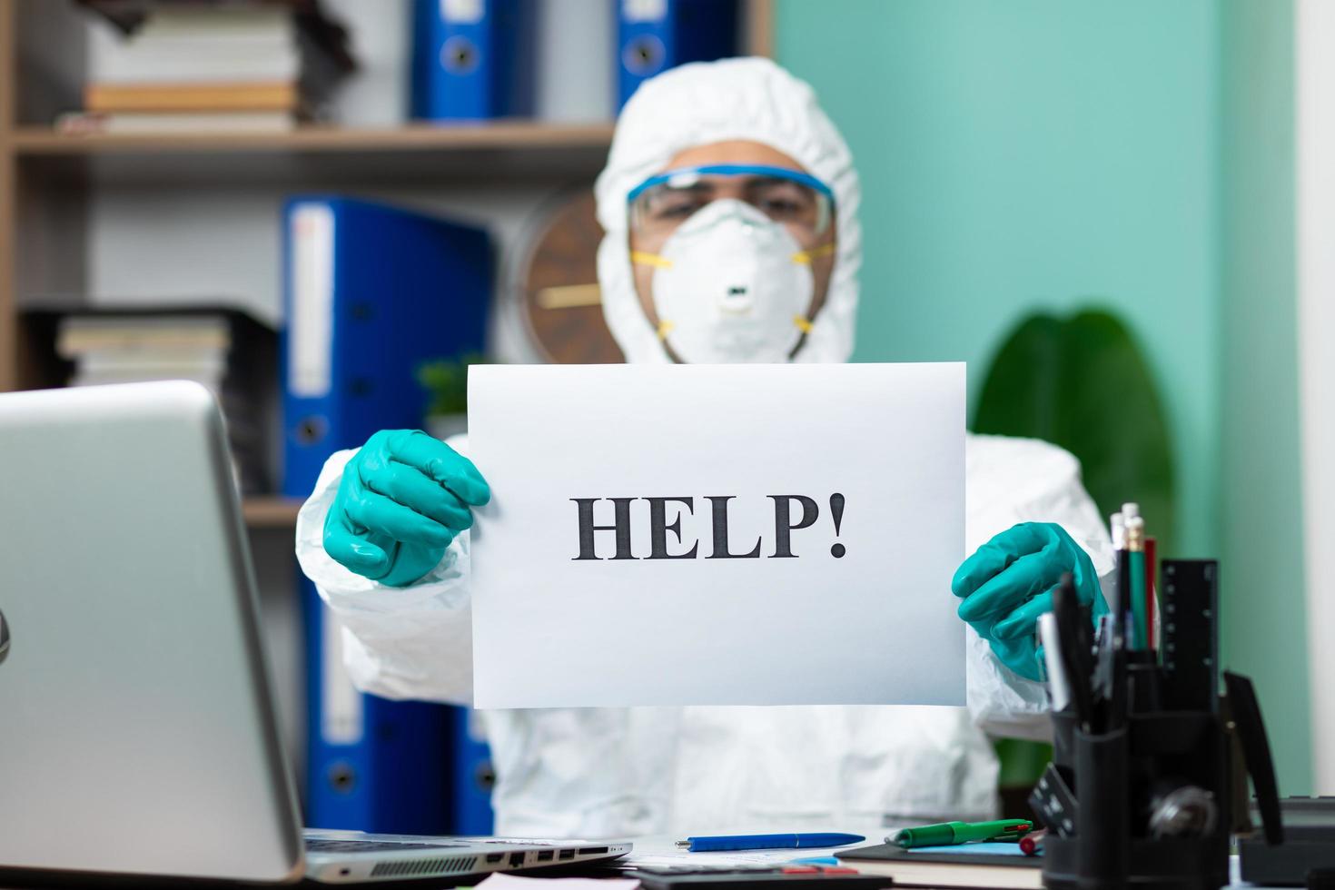 Person in protective suit holding help word at office photo