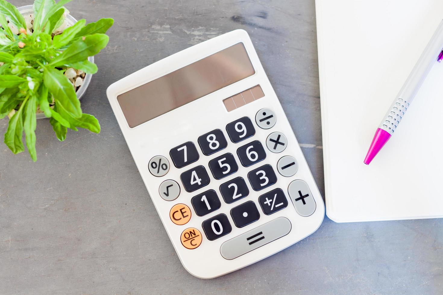 Calculator, notepad, and pen with a green plant photo