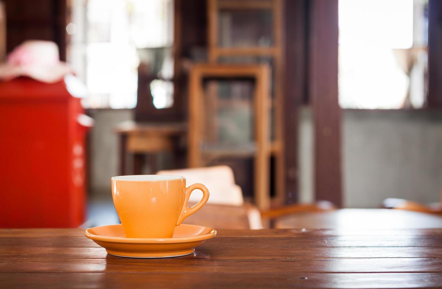 Taza de café naranja sobre una mesa de madera en una cafetería. foto