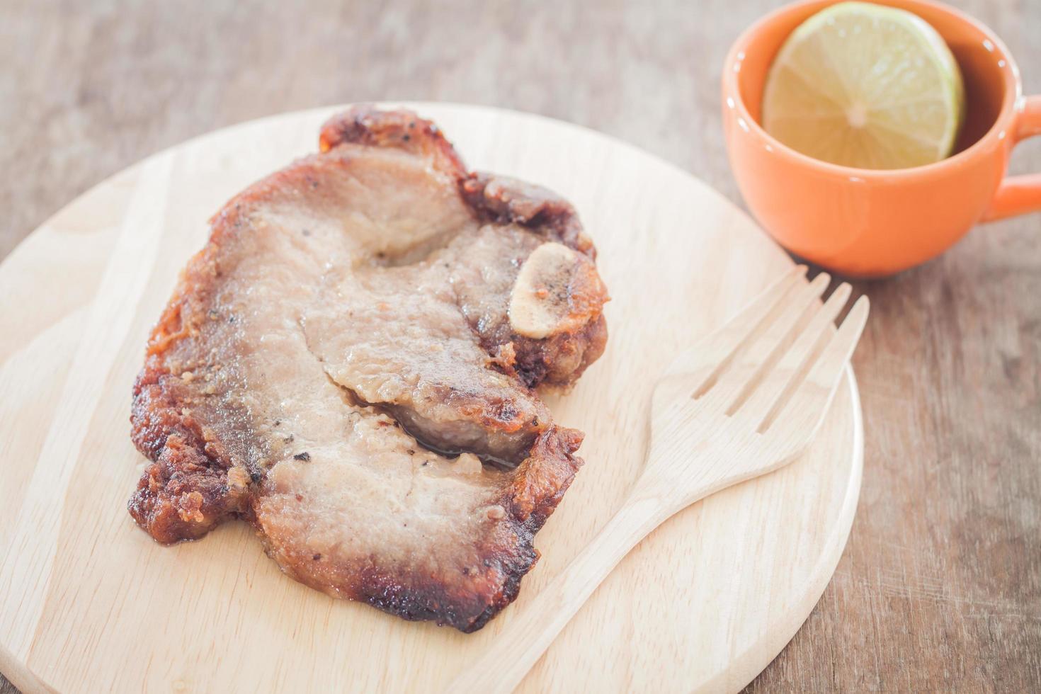 Pork steak on a wooden plate with a cup of lime photo