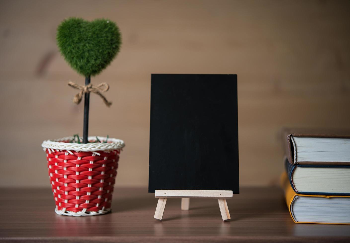 Small chalkboard with heart-shaped plant and books photo