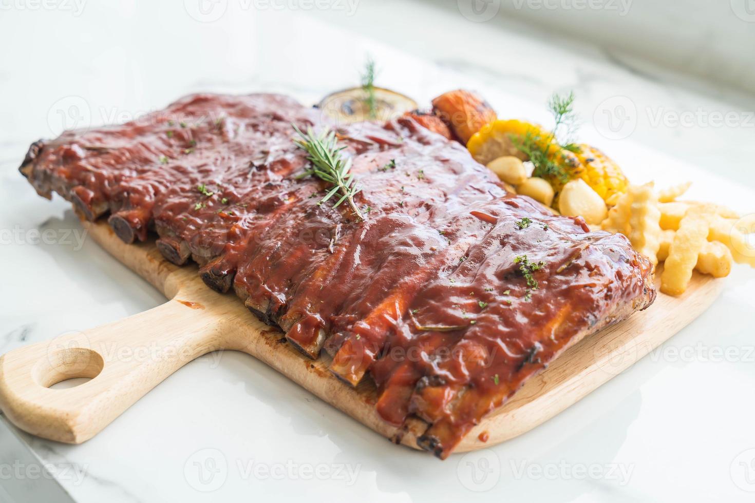 Grilled BBQ ribs with vegetables and french fries on wooden cutting board photo