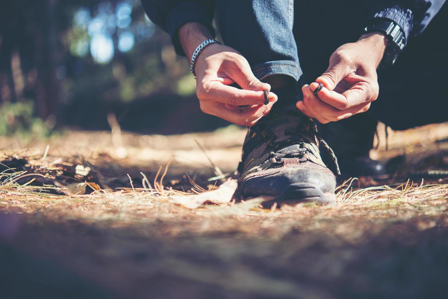 Hombre joven excursionista ata los cordones de sus zapatos mientras viaja con mochila en el bosque foto