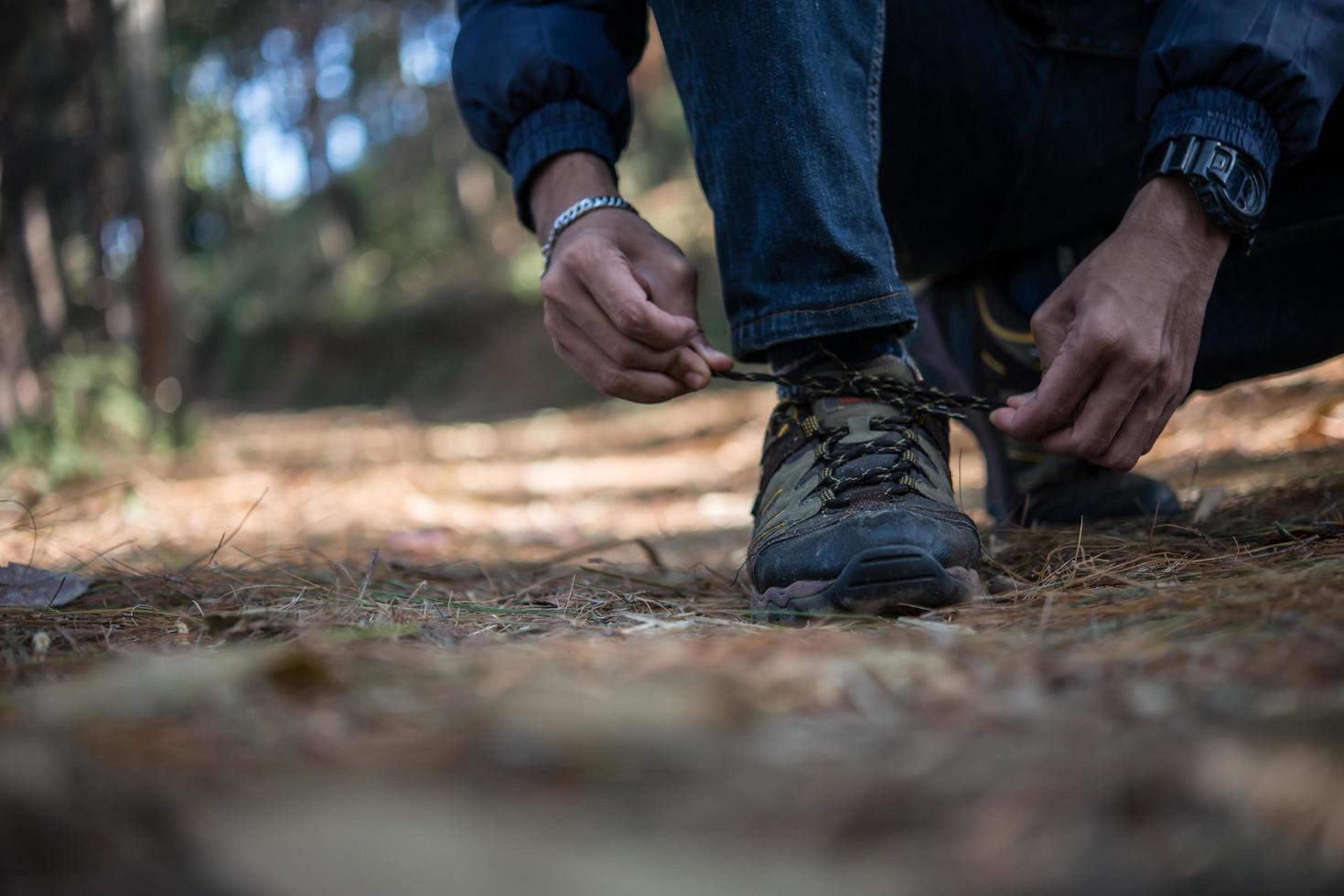 Hombre joven excursionista ata los cordones de sus zapatos mientras viaja con mochila en el bosque foto