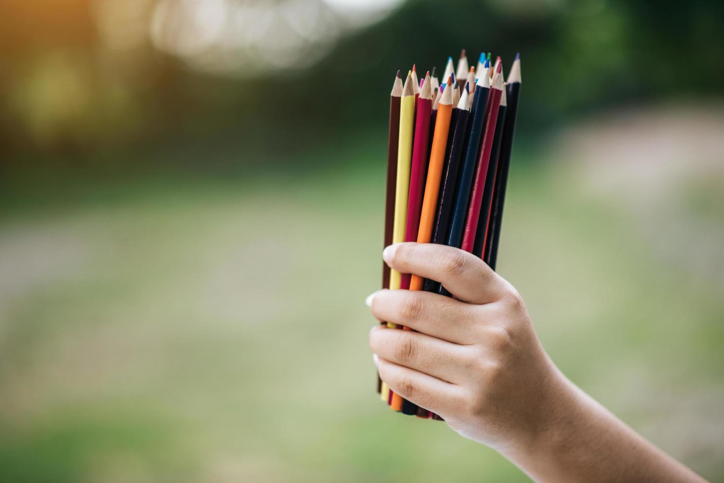 Colorful pencils in hand on green background photo