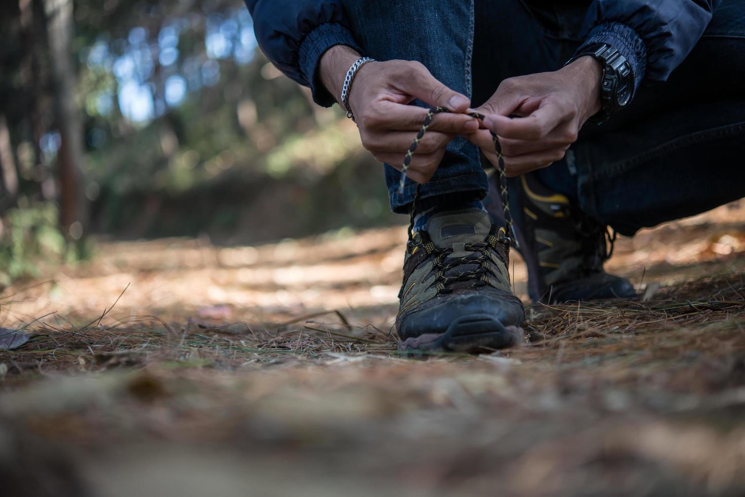 Young hiker man ties his shoe laces while backpacking in the forest photo