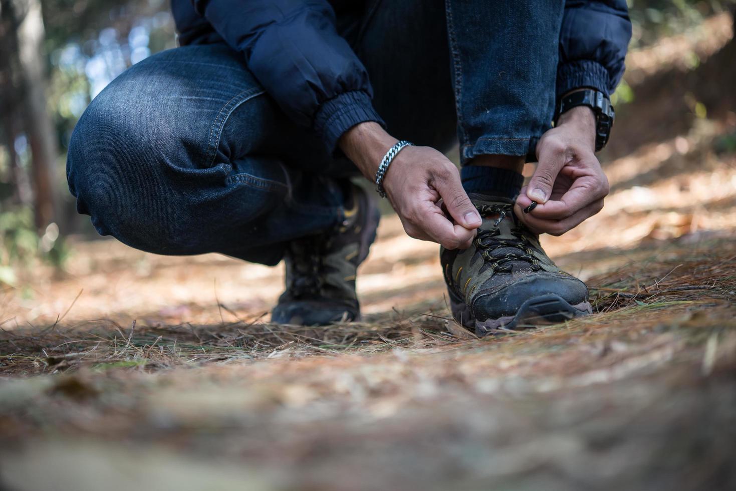 Hombre joven excursionista ata los cordones de sus zapatos mientras viaja con mochila en el bosque foto